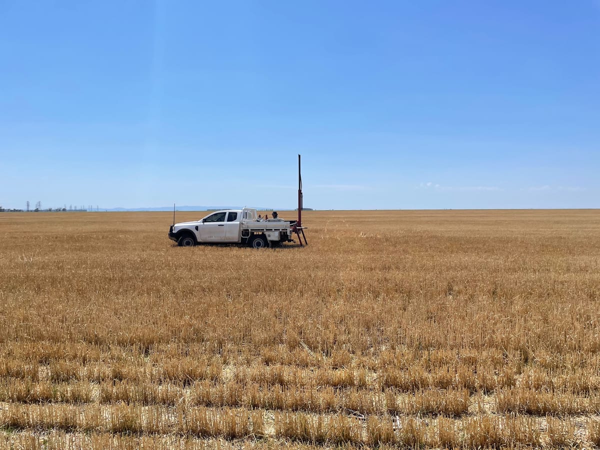 A ute in the middle of a vast, harvested wheat field with a soil sampling machine in the tray.