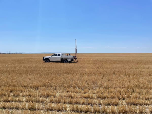 A ute in the middle of a vast, harvested wheat field with a soil sampling machine in the tray.